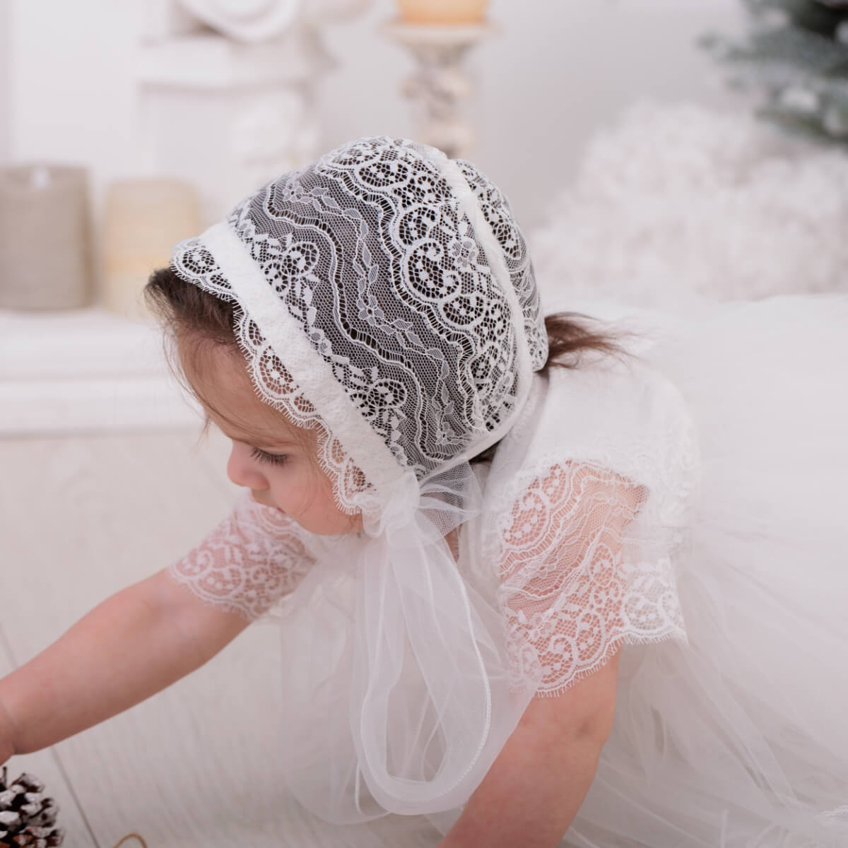 Child wearing a Lace Baptism Bonnet and dress in a cozy indoor setting