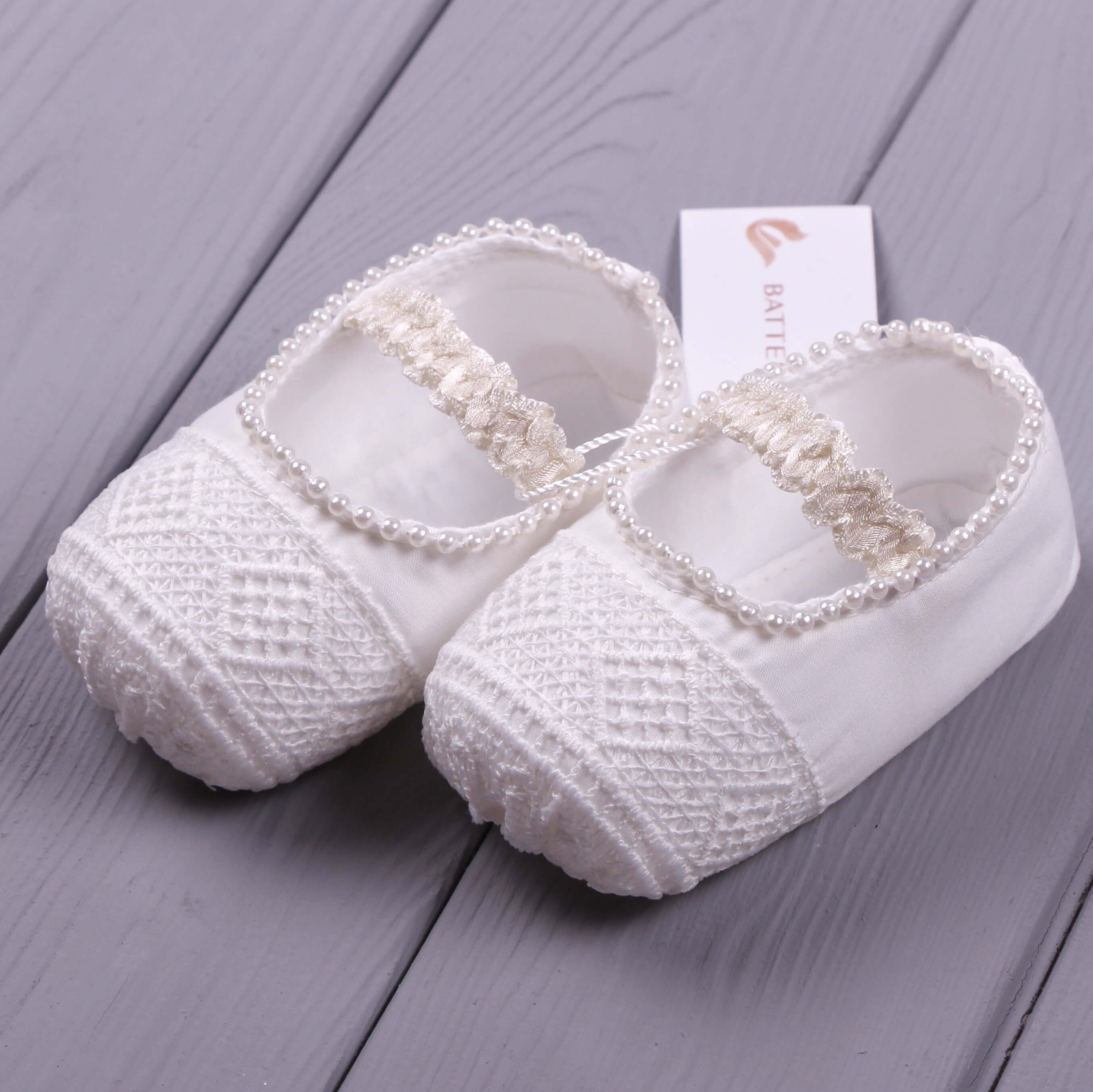 Christening Booties with pearl embellishments on a gray wooden surface