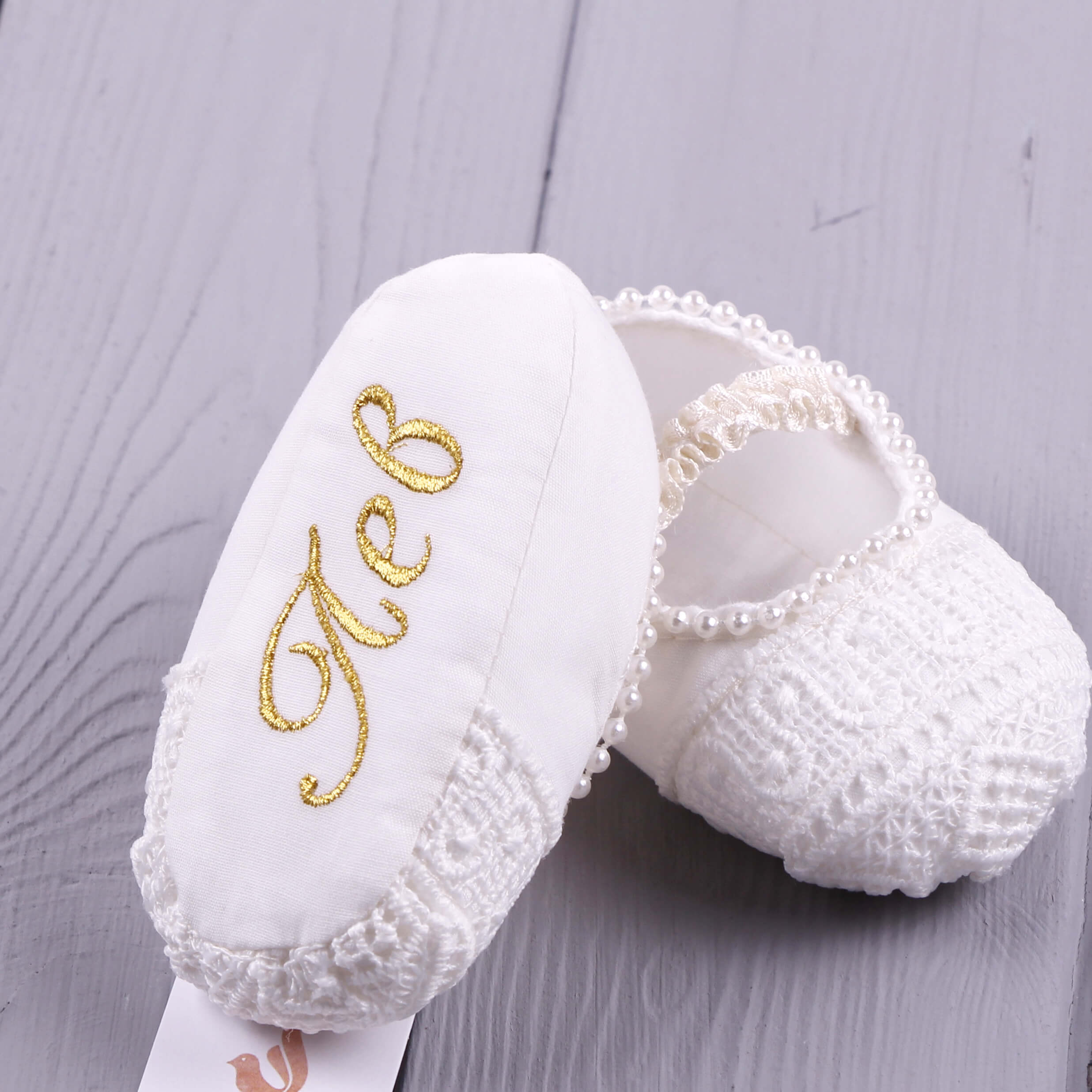 Christening Booties with gold embroidery on a gray wooden surface