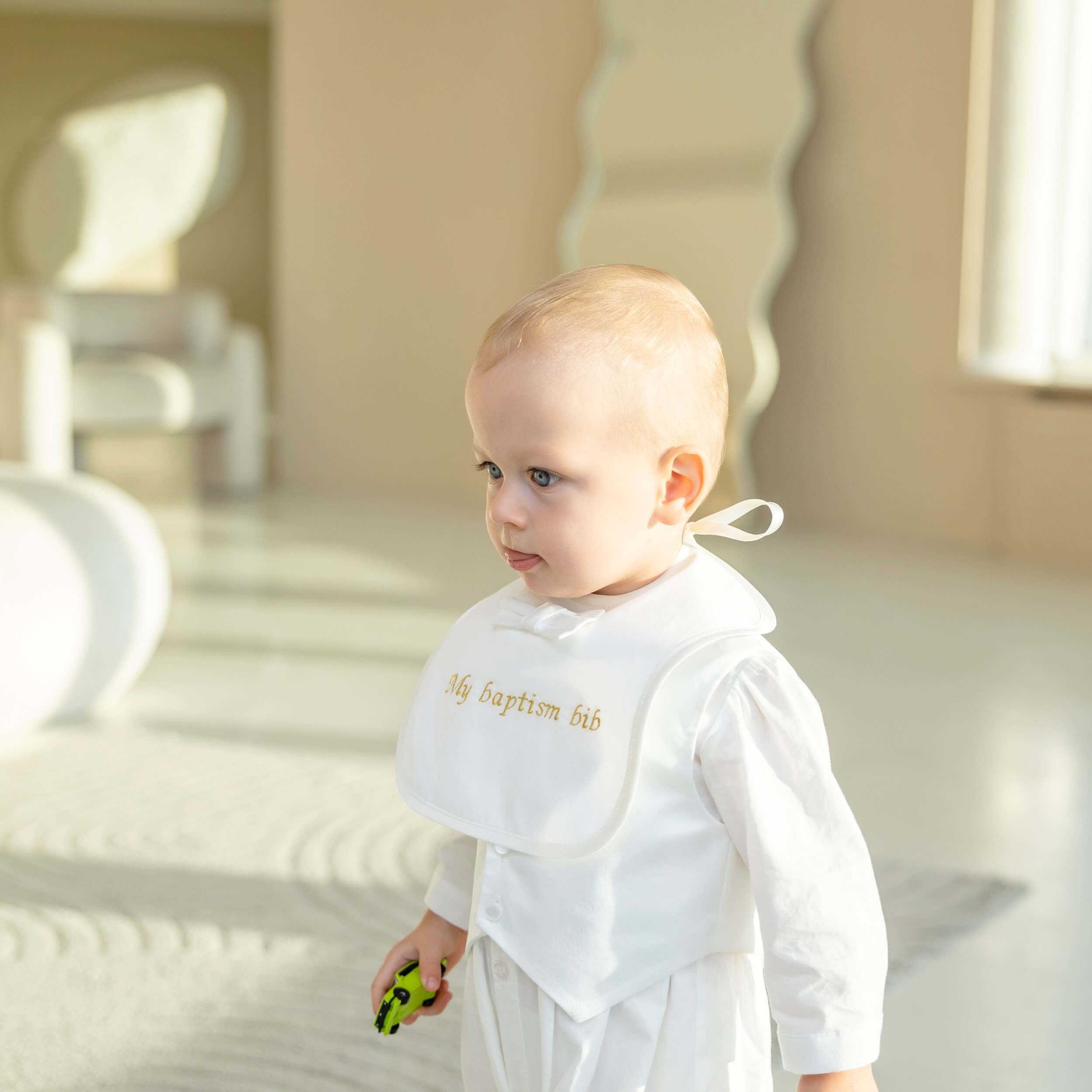 Baby wearing a white baptismal outfit with a Baptism Bib in an outdoor setting.