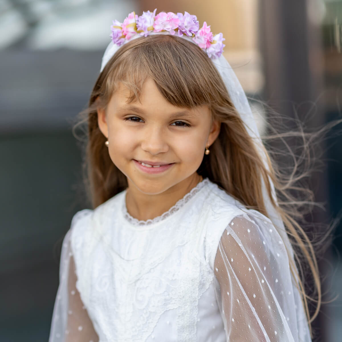 Young girl in a white Traditional Communion Dress with a floral headband, smiling outdoors.