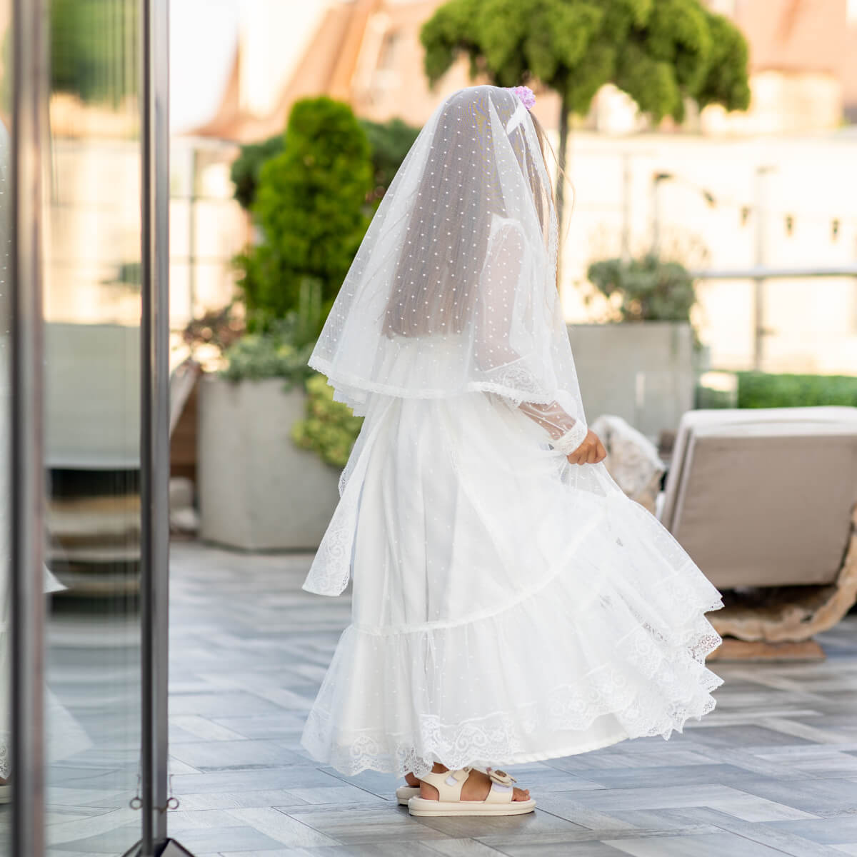 Person wearing a white Traditional Communion Dress with a polka dot veil outdoors.