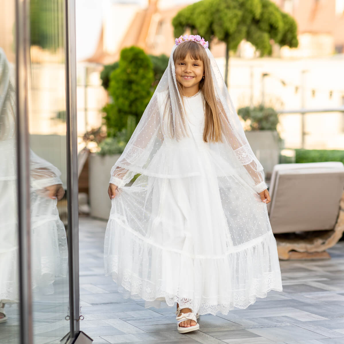 Young girl in a white Traditional Communion Dress with a veil standing outdoors.
