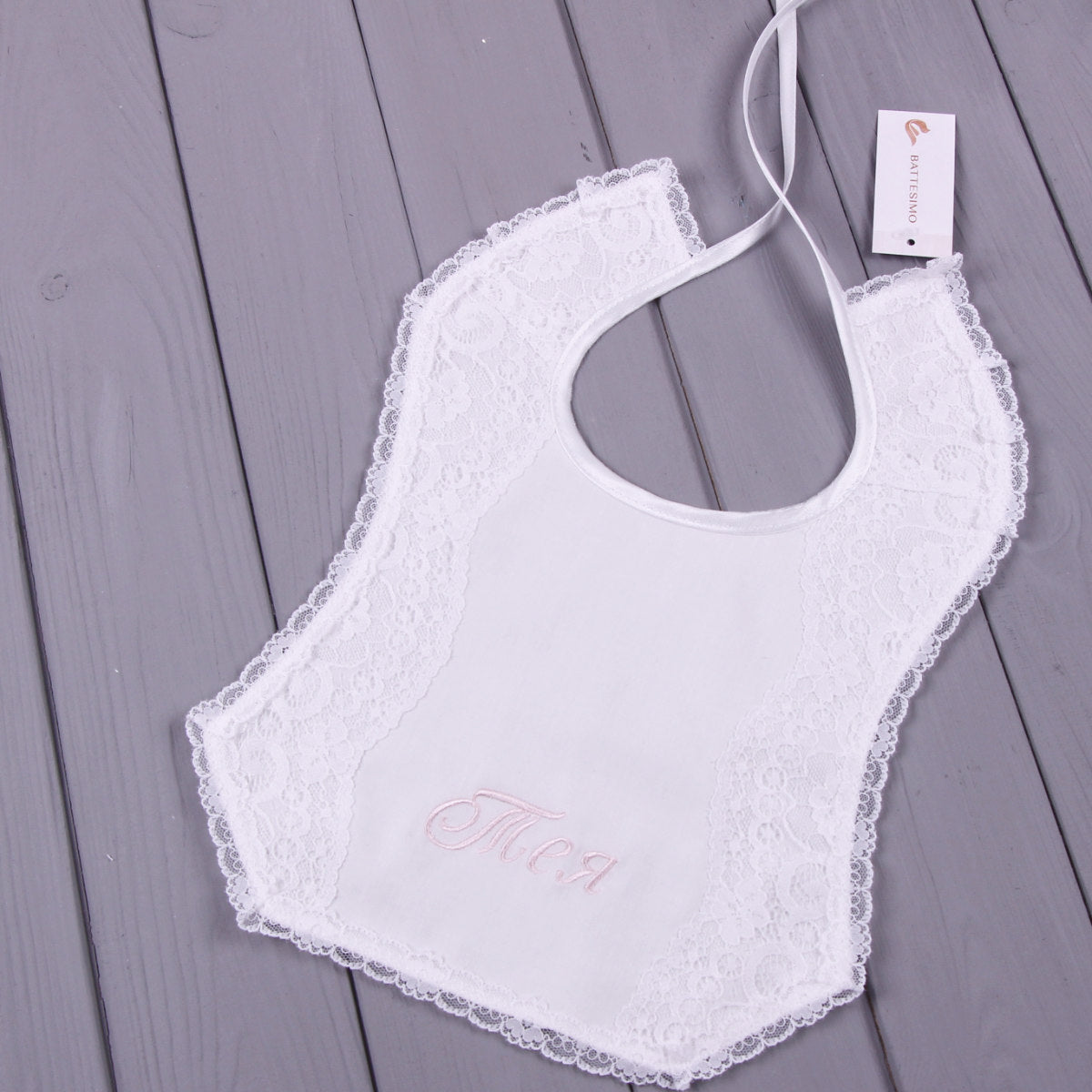 White lace Baptism Bib with 'Mia' embroidery on a gray wooden surface