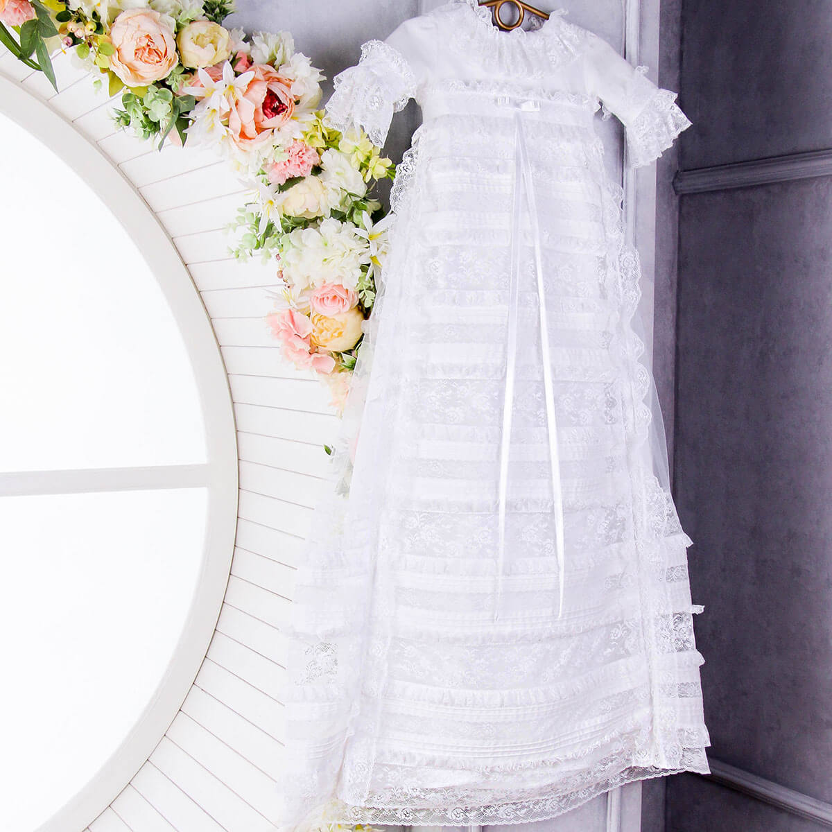 White lace dress hanging on a rack with floral decorations in the background