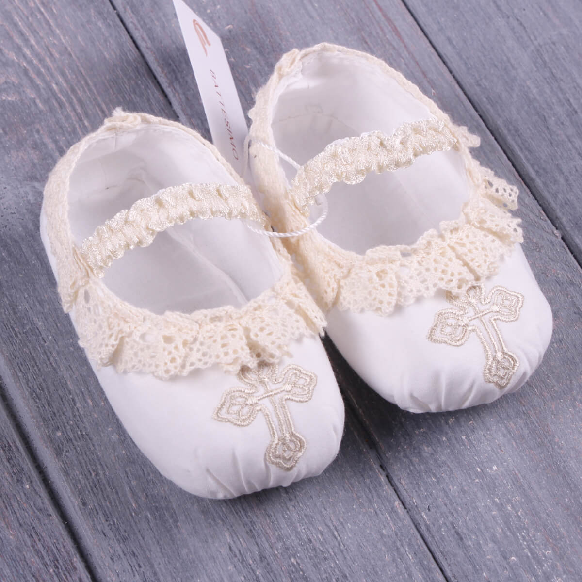 Christening Booties with lace and cross embroidery on a wooden surface