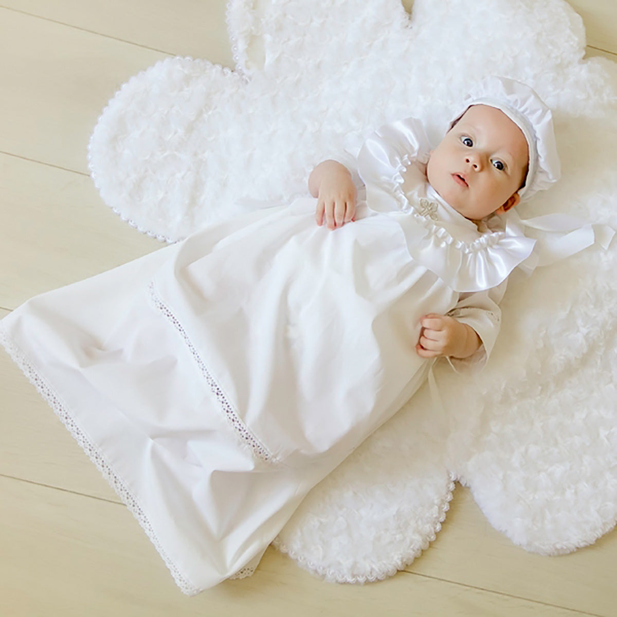 Baby in a white christening long gown and bonnet lying on a textured white blanket