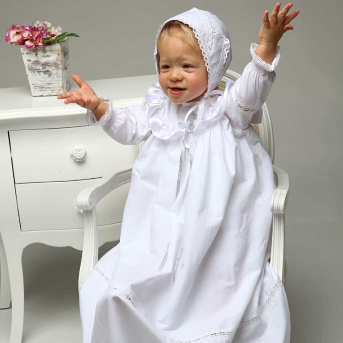 Christening Gown for Girls with a hood sitting on a chair against a gray background