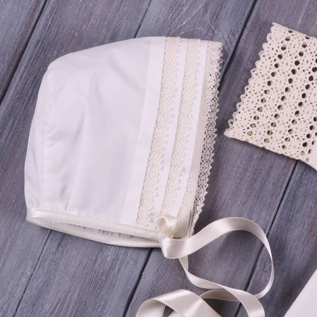 Baby Christening Bonnet with lace trim and ribbon on a wooden surface