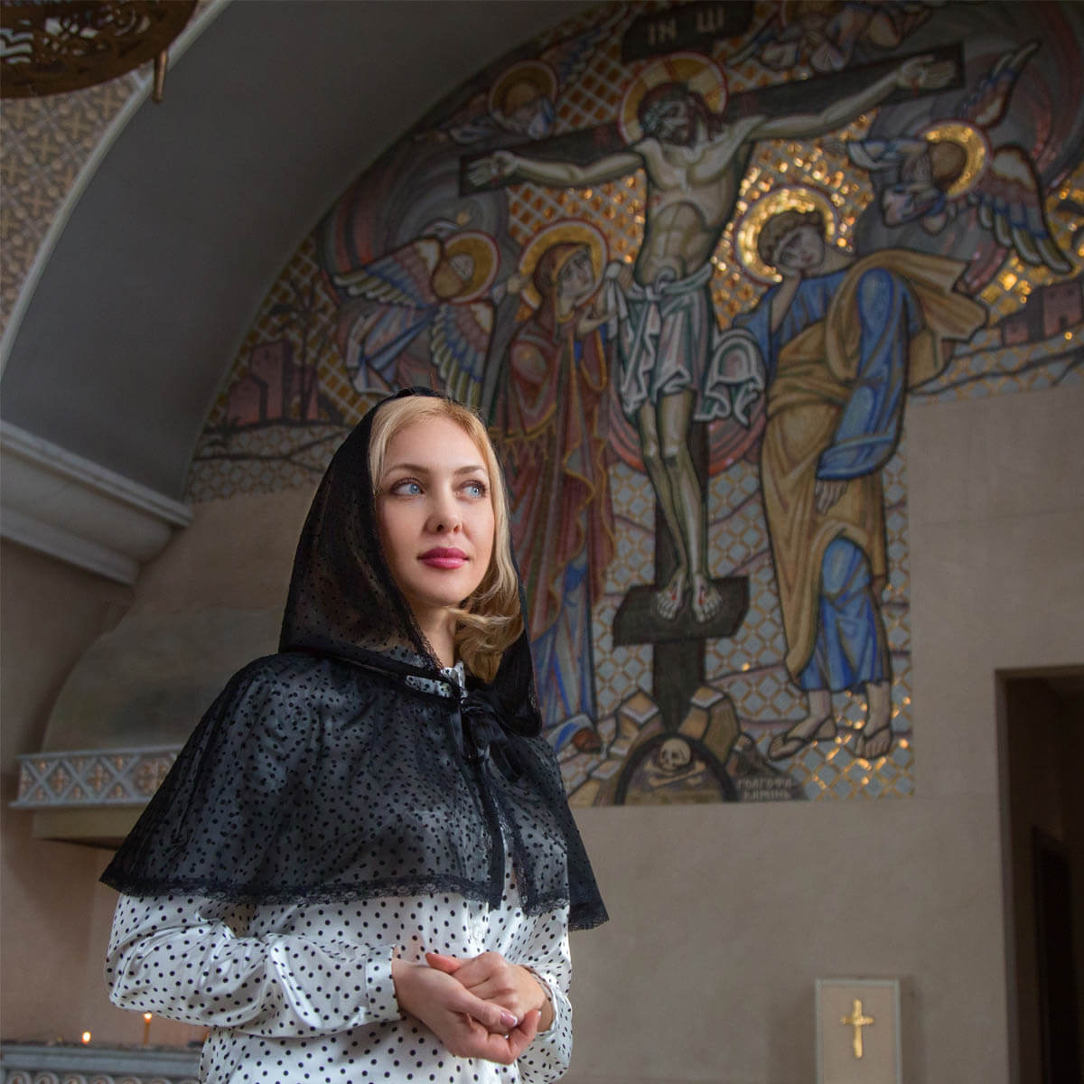 Woman in a Mantilla Chapel Veil standing in front of a religious mural in a church.