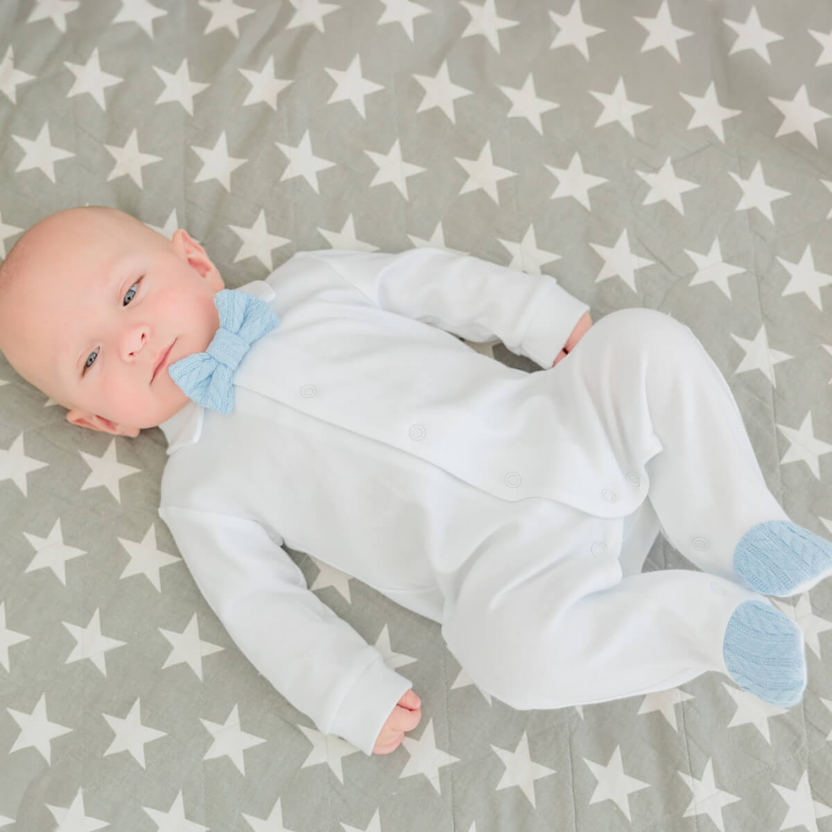 Baby in a Newborn Coming Home Outfit with blue accents lying on a gray blanket with white star pattern
