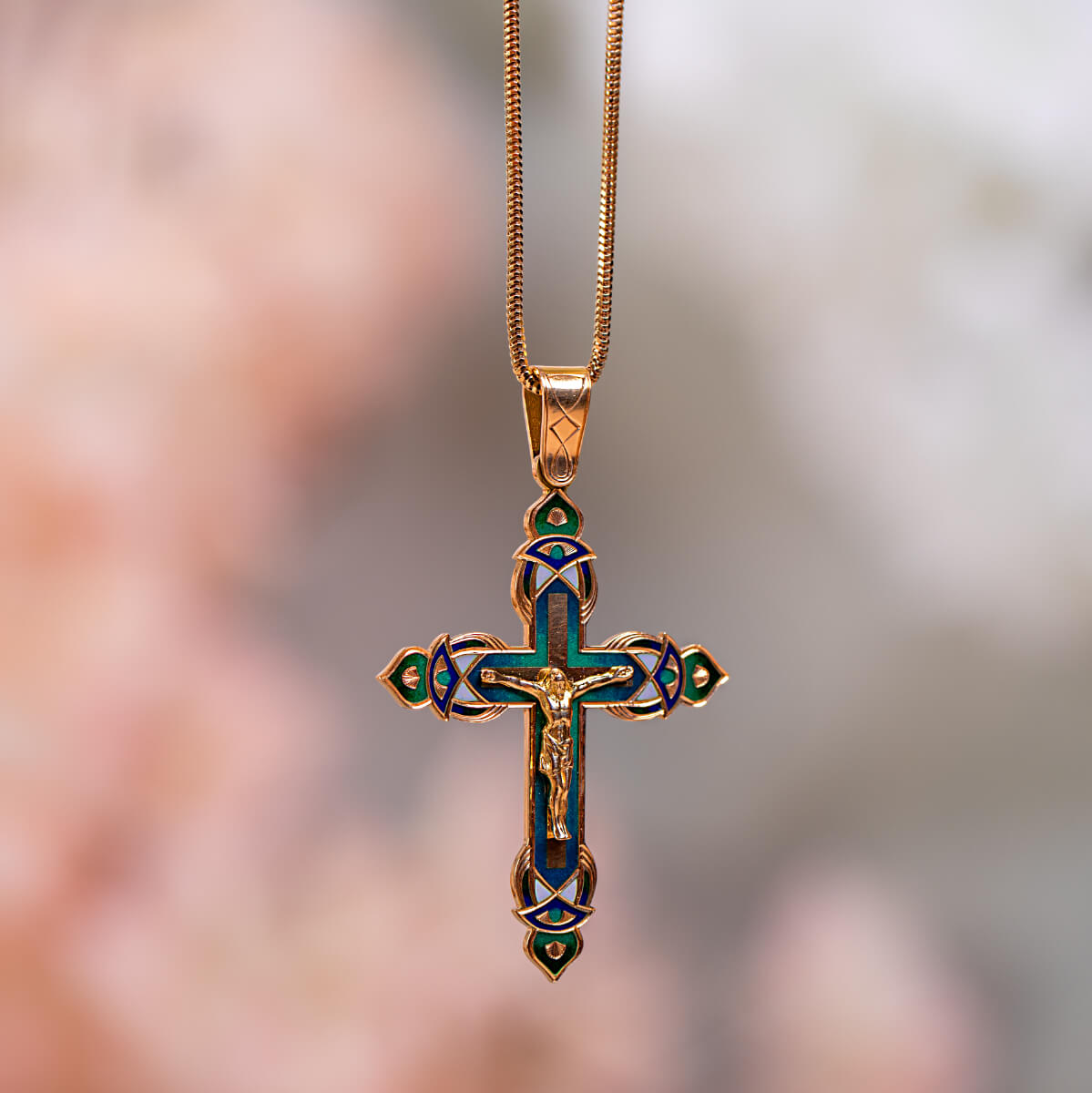 Gold cross pendant with enameled details on a blurred background