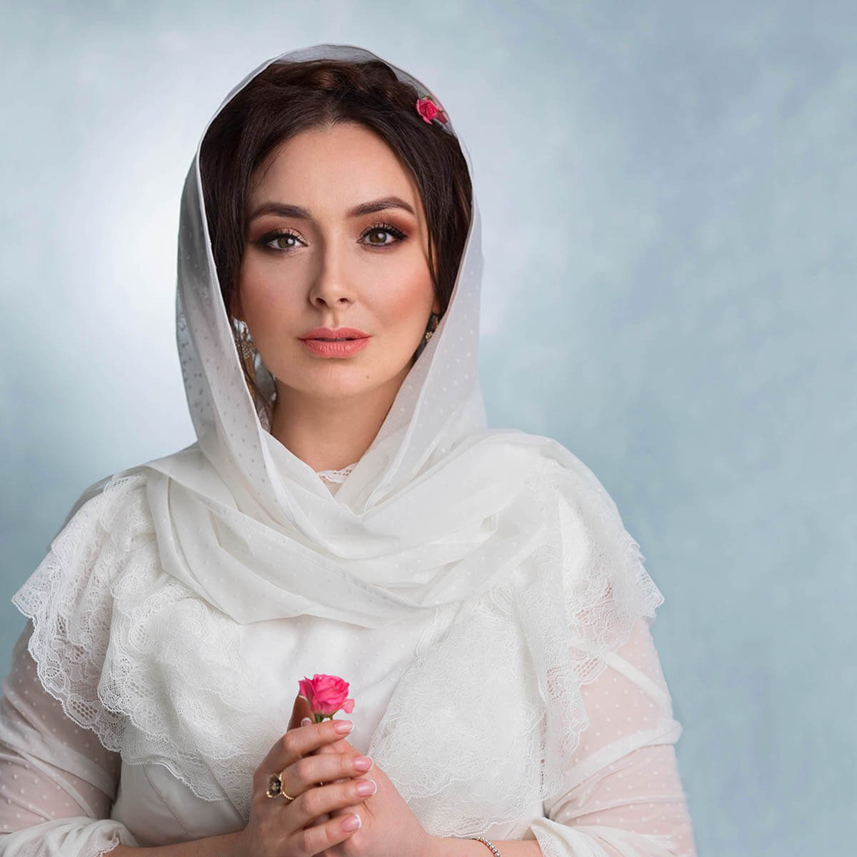 Woman wearing a Tulle Chapel Veil holding a pink rose against a light blue background