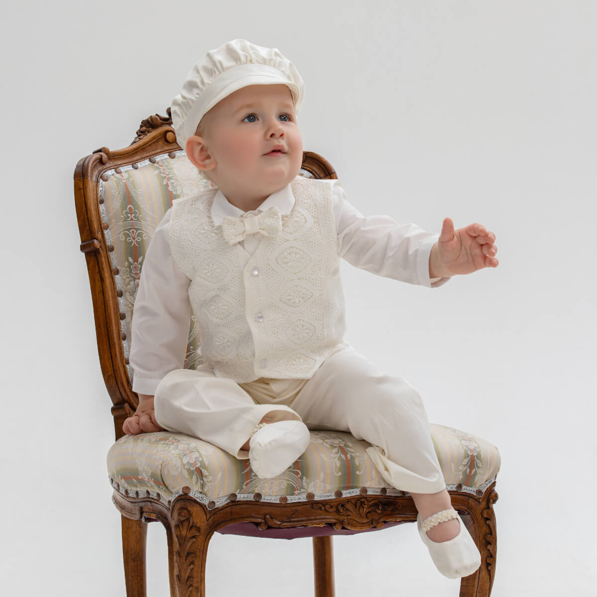 Baby in Baby Boy Baptism Suit sitting on a decorative chair against a plain background