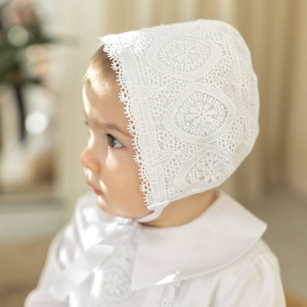 Baby wearing a Boy Baptism Hat in a softly blurred indoor setting