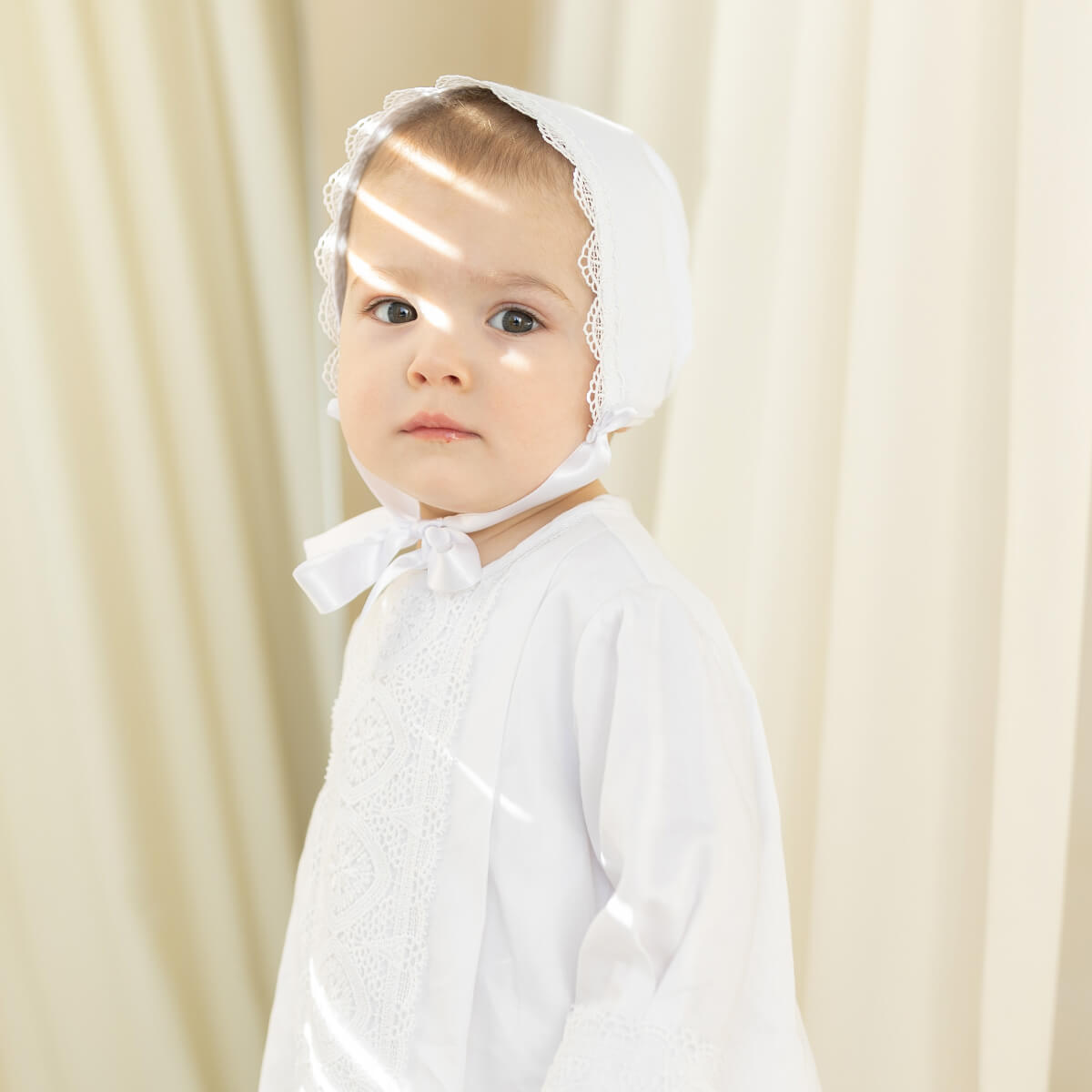 Baby wearing a Boy Baptism Hat against a beige curtain background