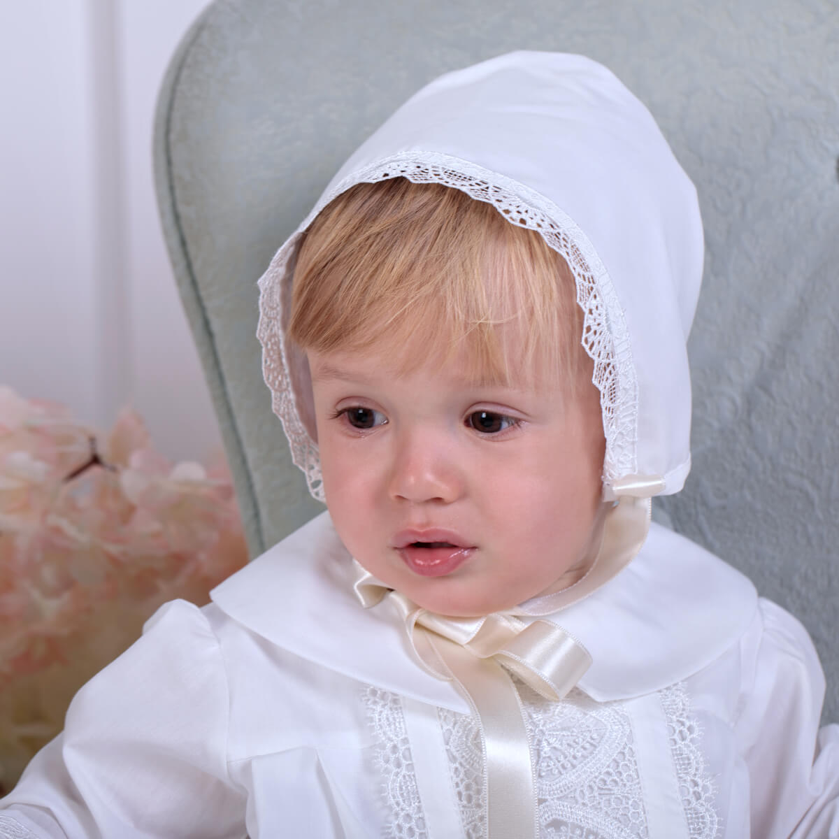 Baby wearing a Boy Baptism Hat with lace details against a neutral background