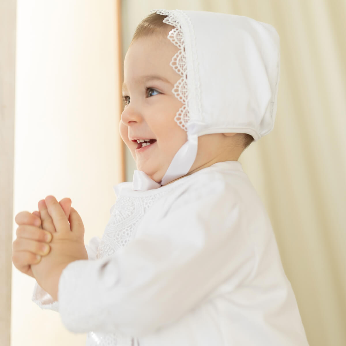 Baby wearing a Boy Baptism Hat with lace details against a plain background