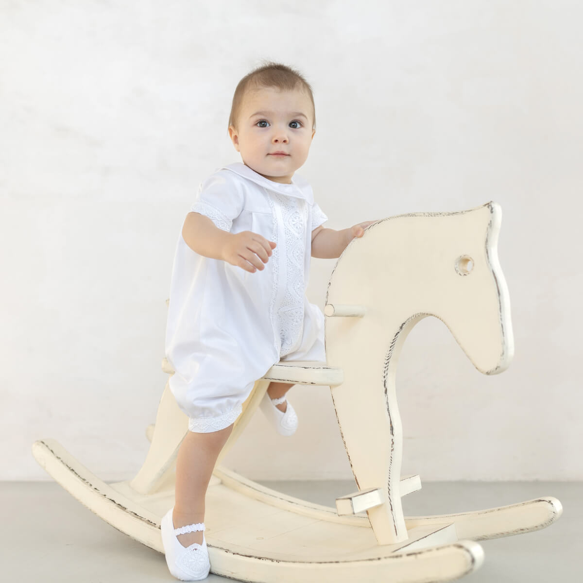 Baby Boy Baptism Romper sitting on a beige rocking horse against a plain background
