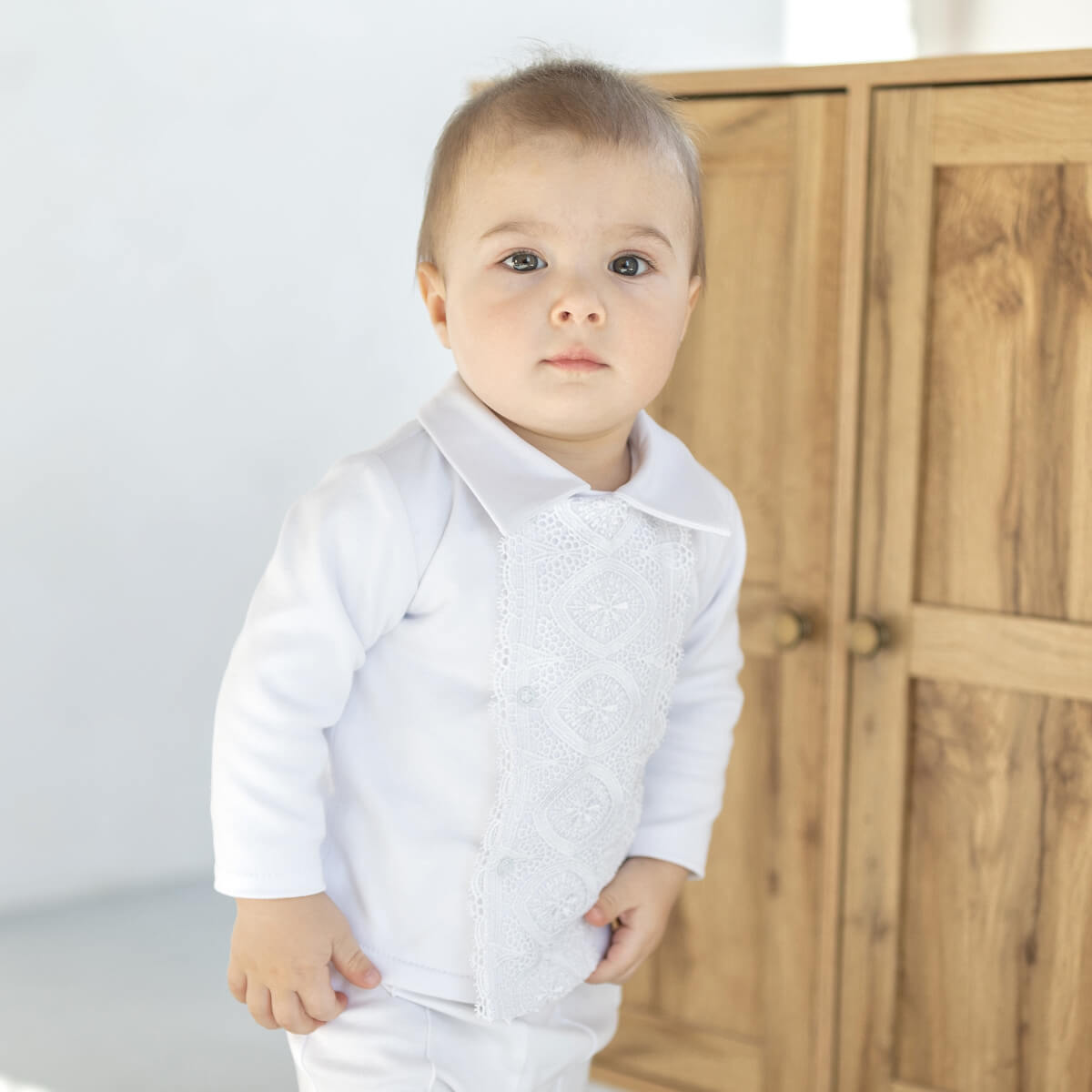 Baby wearing a Baby Boy Baptism Jersey Suit standing in front of a wooden wardrobe.