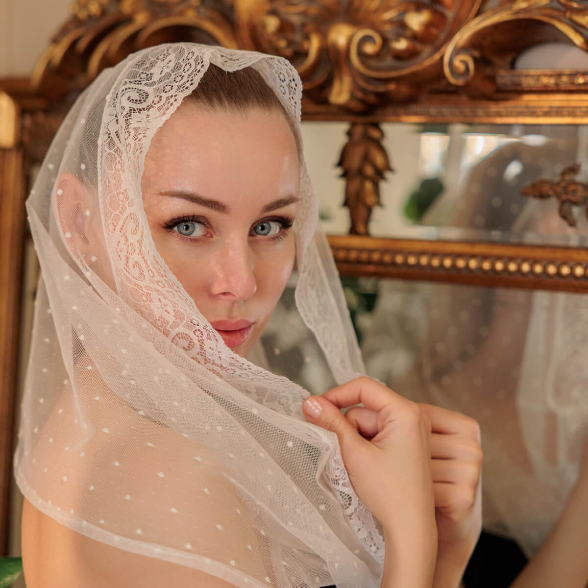 Woman wearing a Catholic Infinity Veil in front of an ornate mirror.