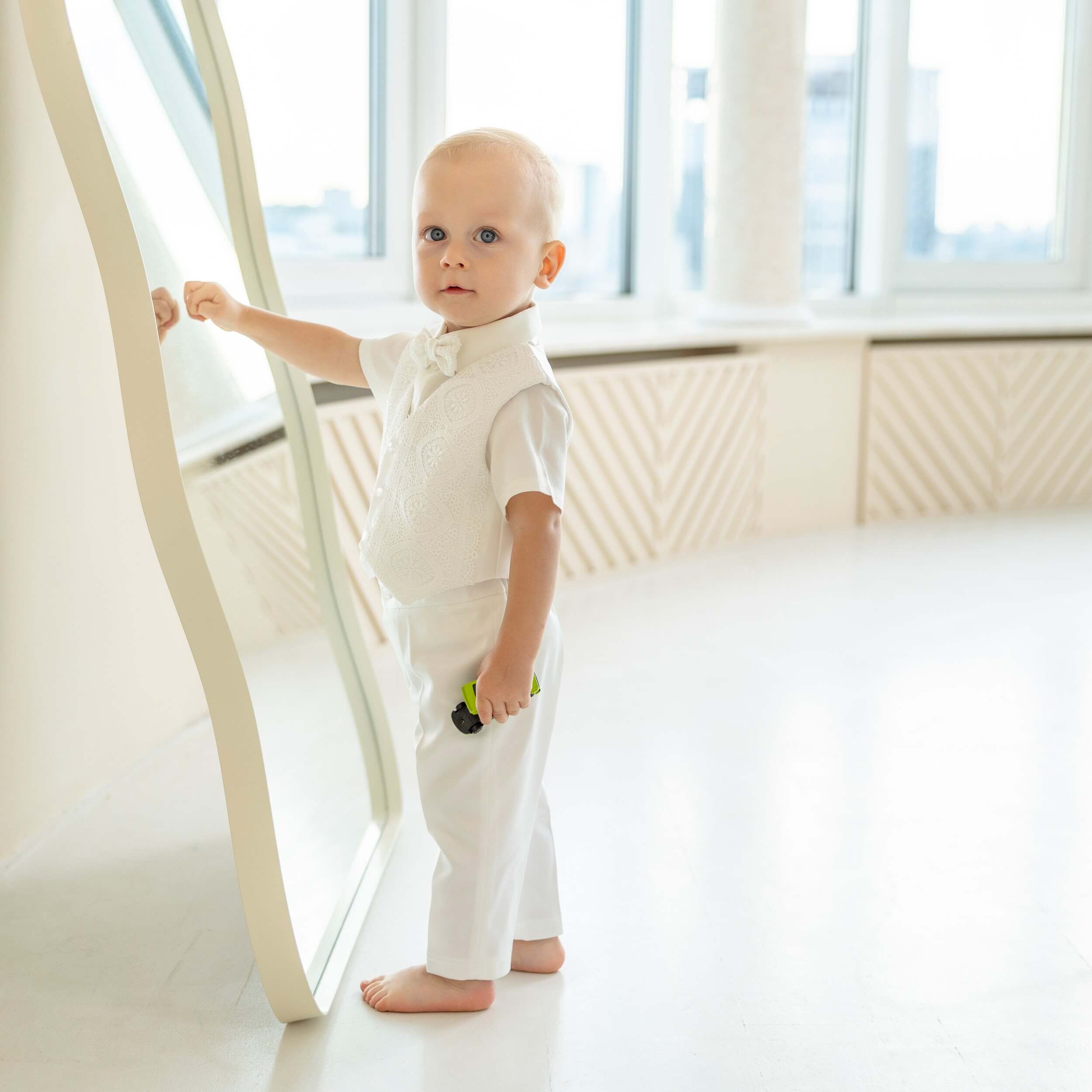 Child in a Baby Boy Baptism Suit standing in a bright room with large windows.