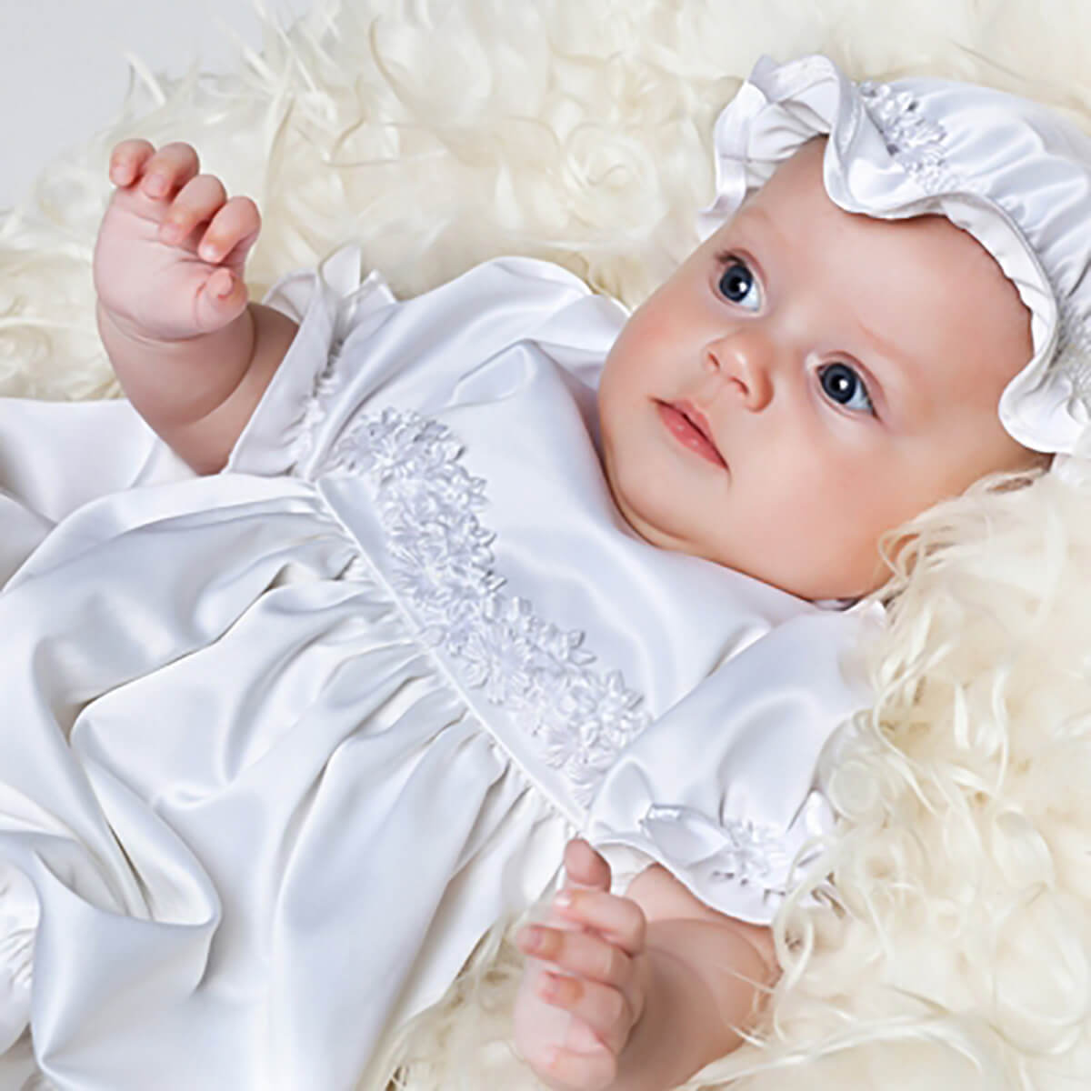 Baby in a Newborn Christening Gown with a bonnet lying on a soft, light-colored surface