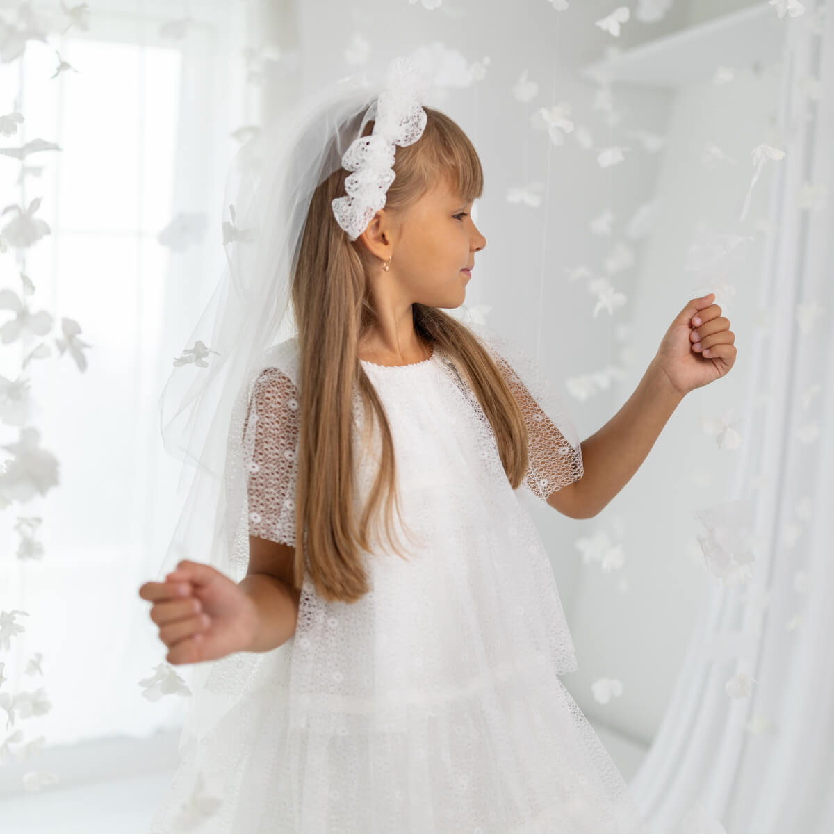 Young girl in Holy First Communion with a headband, standing against a white background.