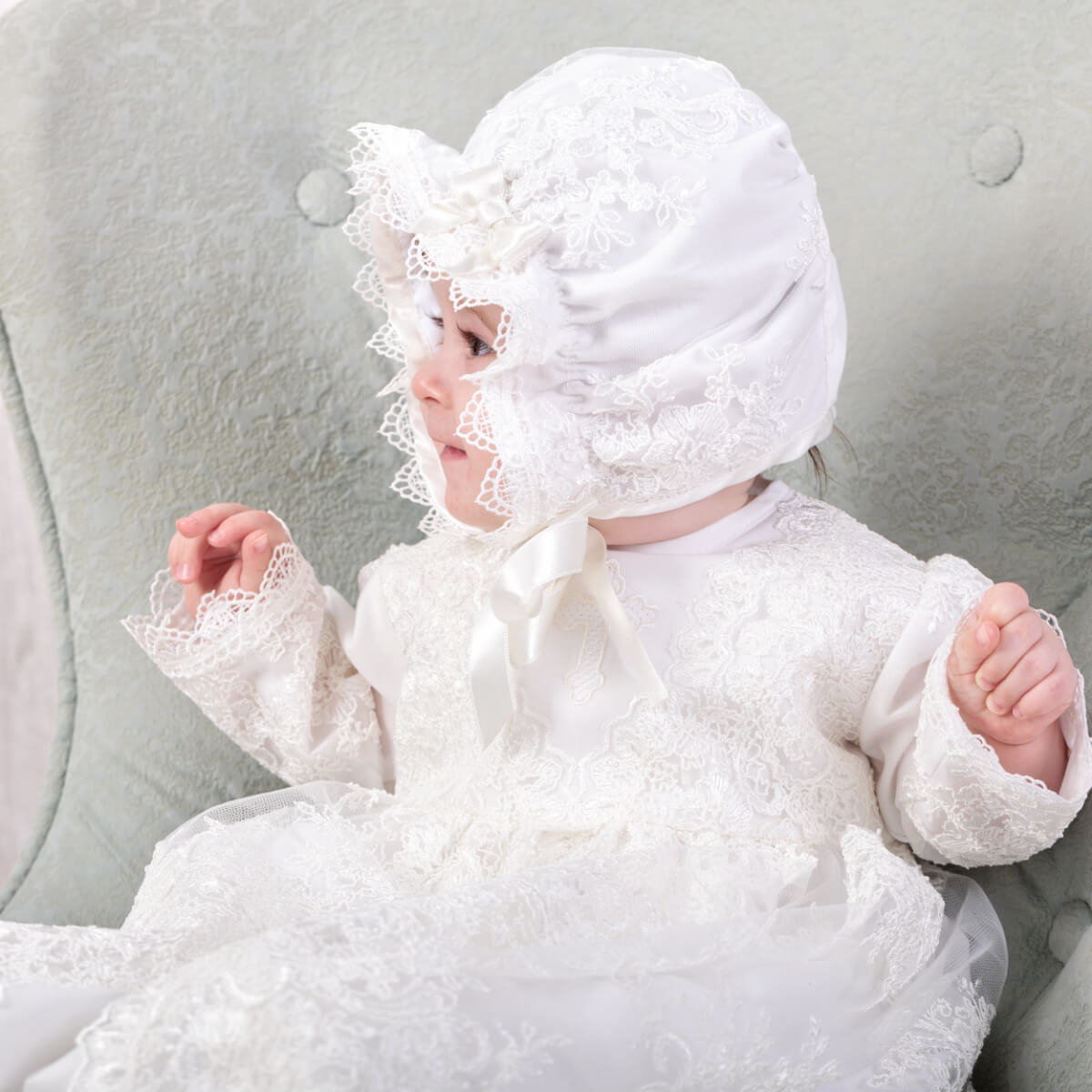 Baby in a Lace Baptism Bonnet sitting on a gray cushion