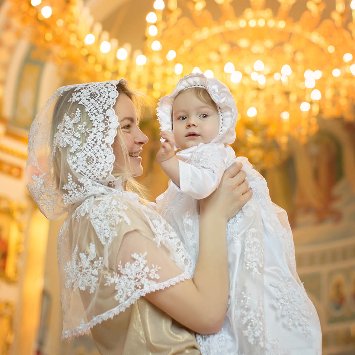 Woman holding a baby in a Lace Hooded Veil indoor setting with lights