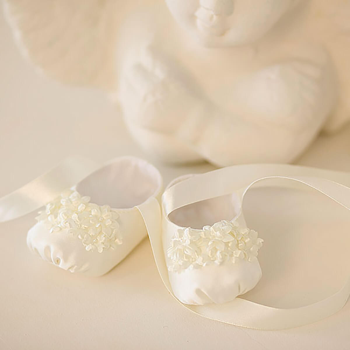 Pair of Christening Booties with floral decorations on a soft beige background