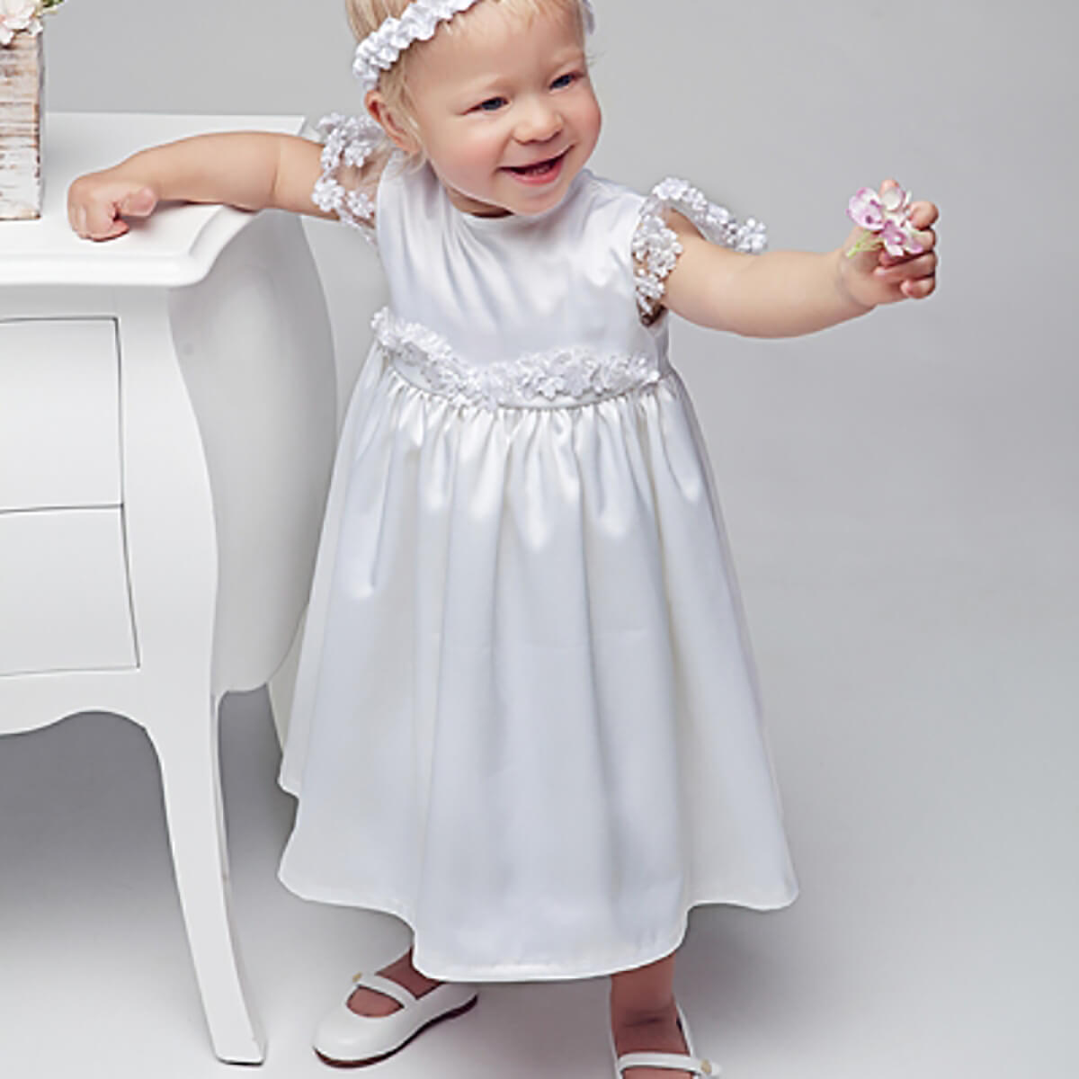 Baby in a Christening Dress with floral details standing on a white surface