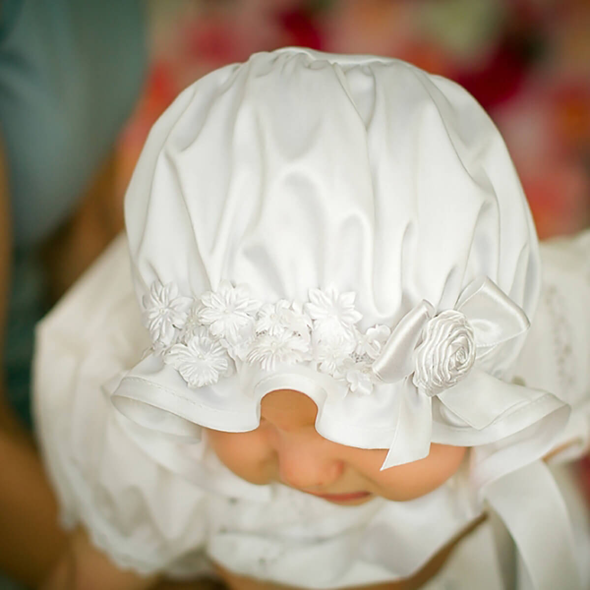 Close-up of a child wearing a white Silk Baptism Bonnet with a blurred background
