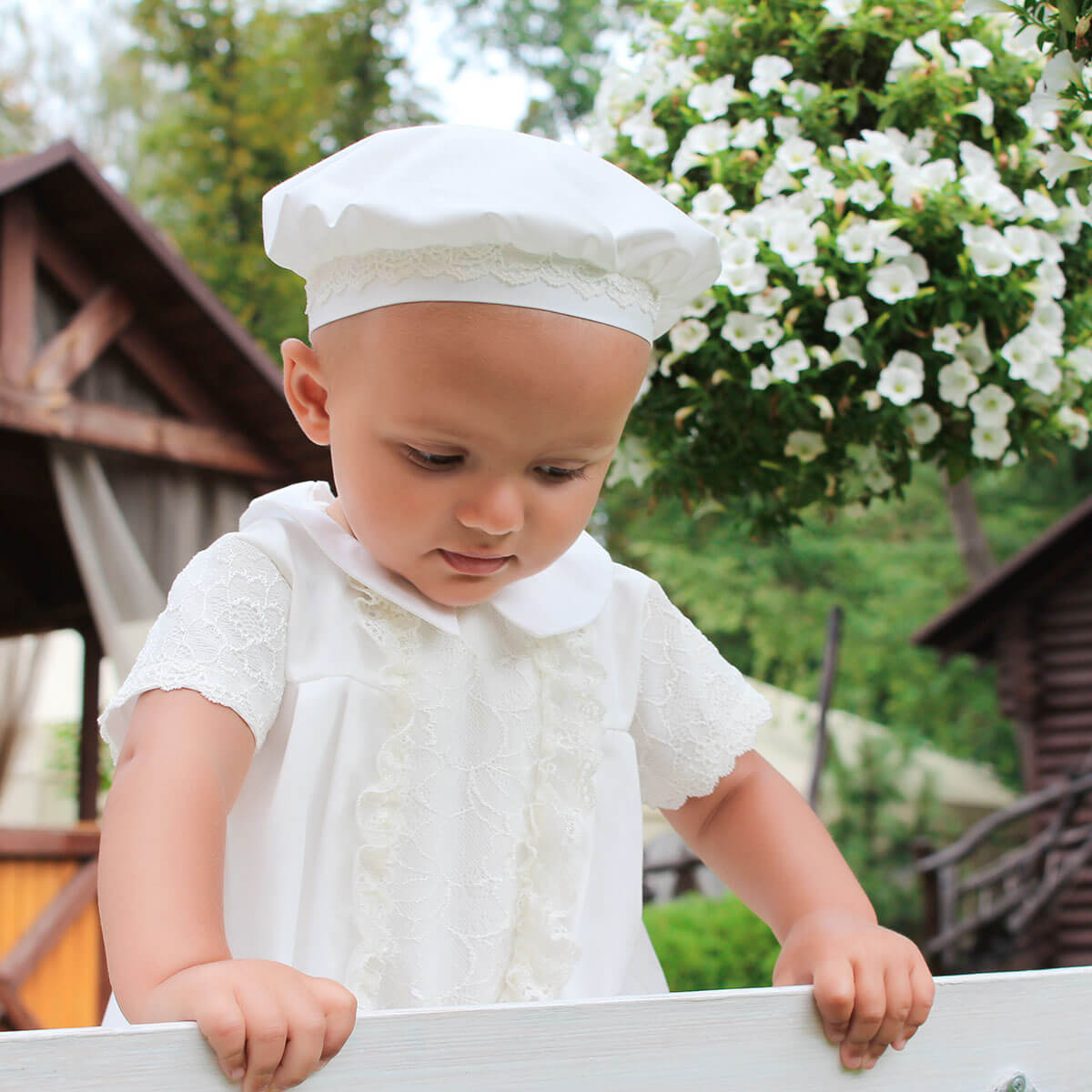 Child in a white outfit with a Boy Christening Hat outdoors