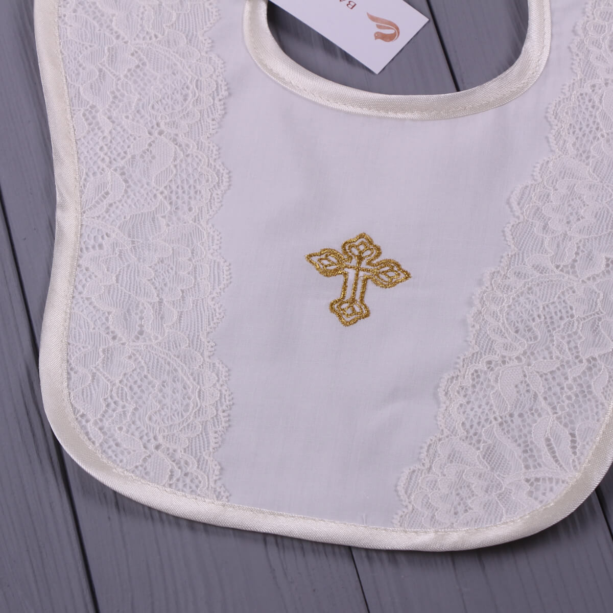 Baptism Bib with lace details and a gold cross on a gray surface
