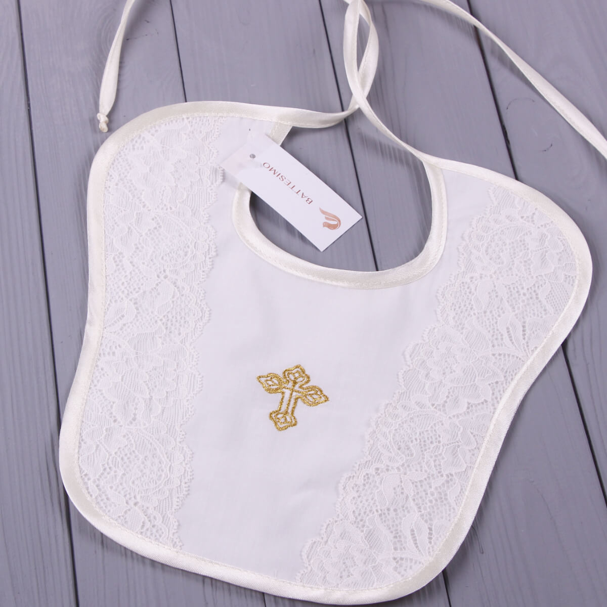 Baptism Bib with gold cross embroidery on a gray wooden surface