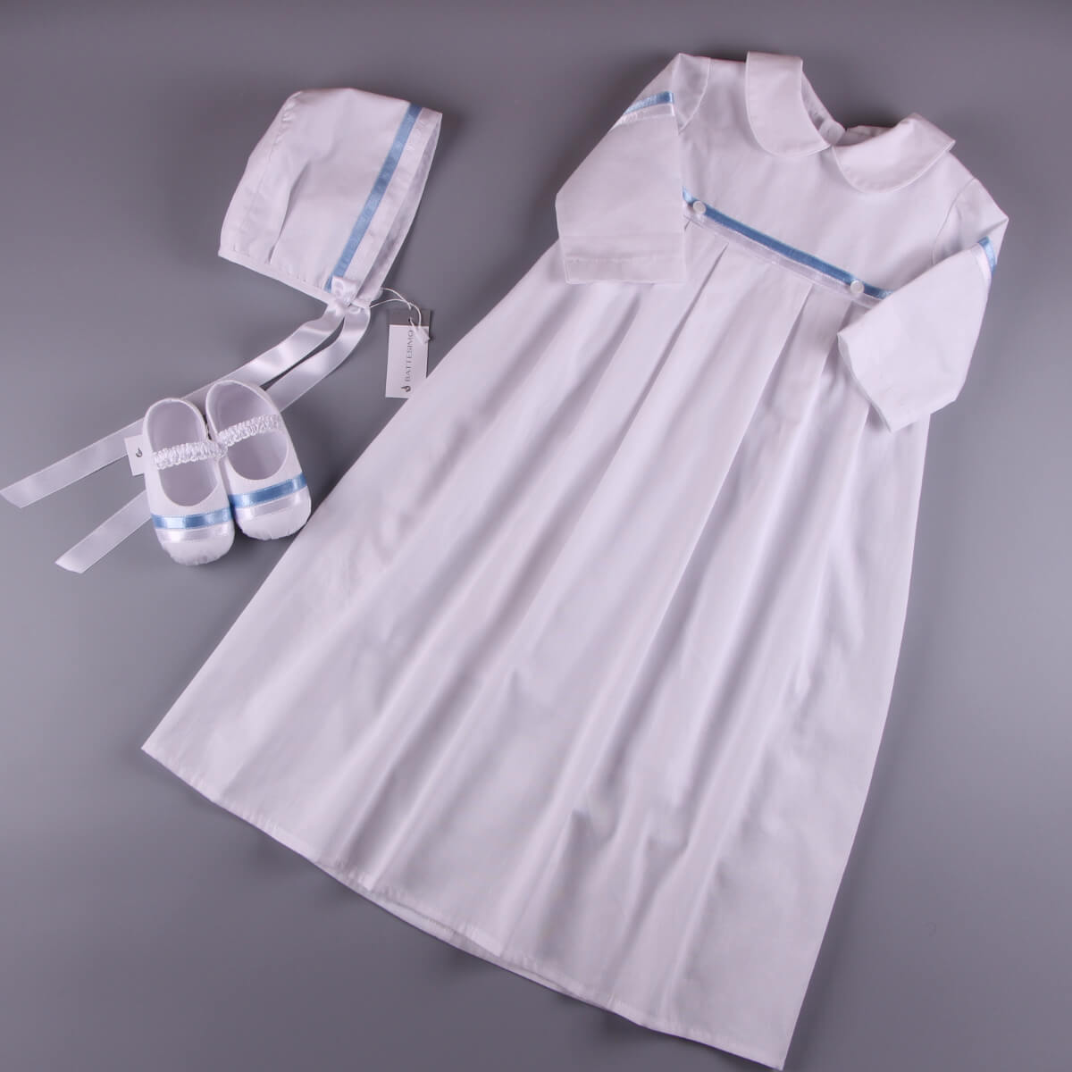 Christening Outfit with blue trim, bonnet, and shoes on a gray background