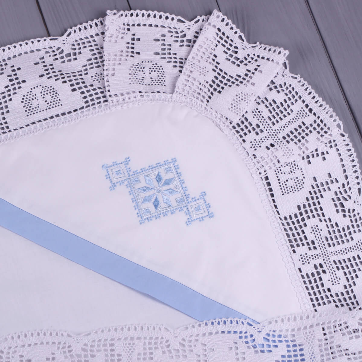 Set of white lace christening blanket with blue embroidery on a wooden surface