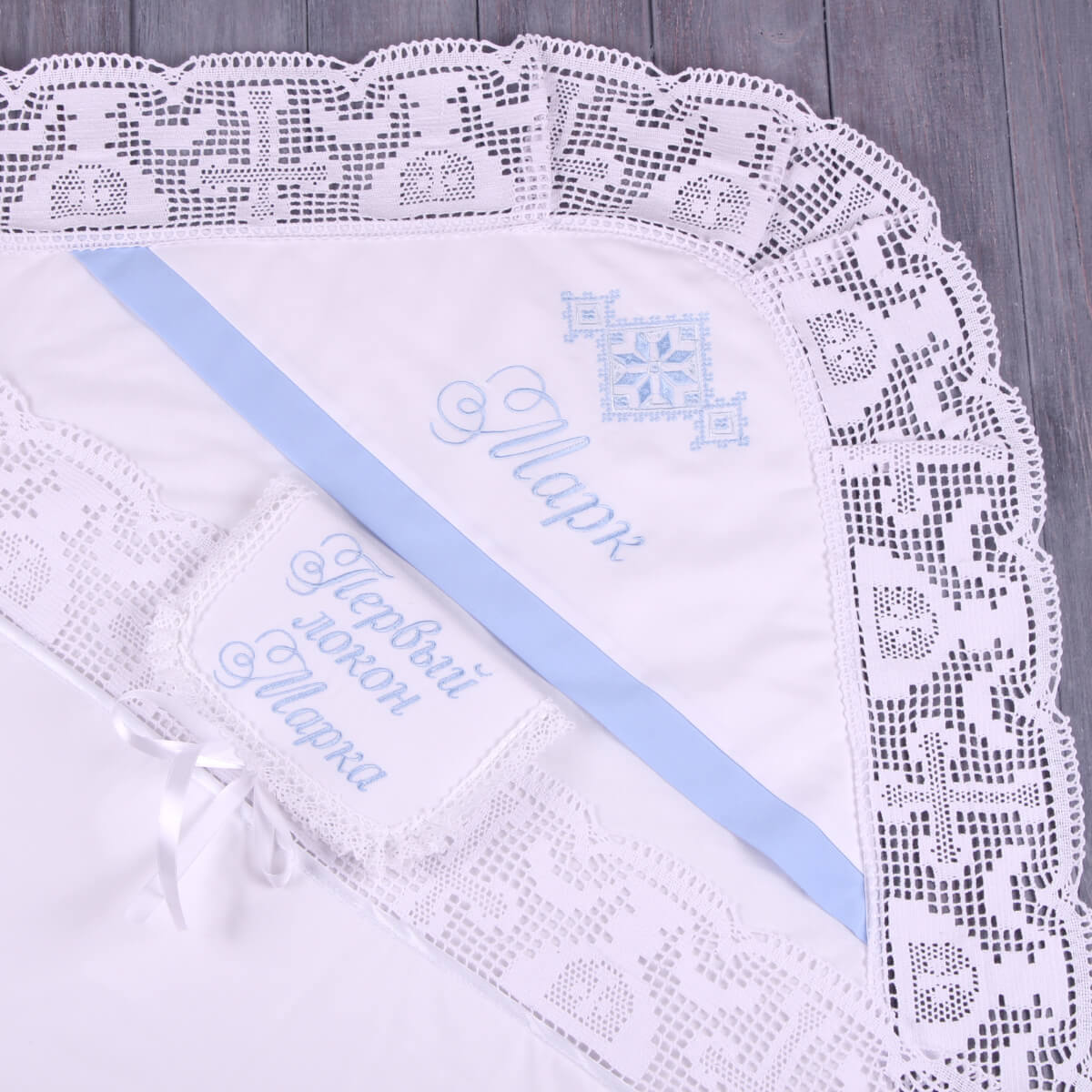 Embroidered baby blanket with lace edge and embroidered text on a wooden surface