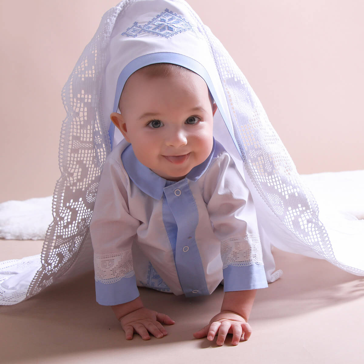 Baby wearing a traditional outfit with a white christening blanket background