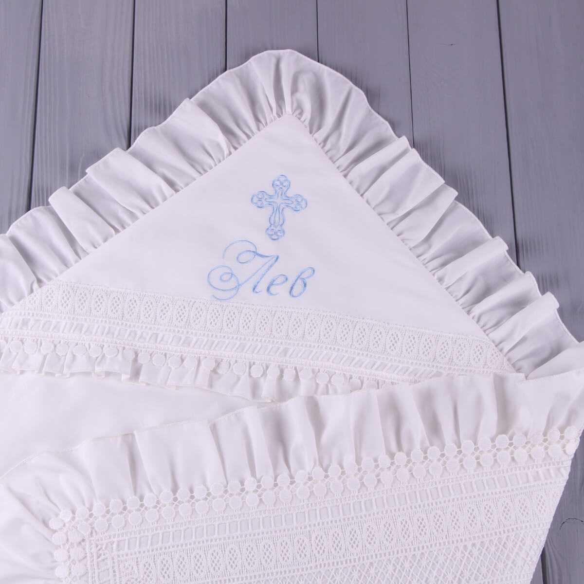 White embroidered christening blanket with a cross and text on a wooden surface