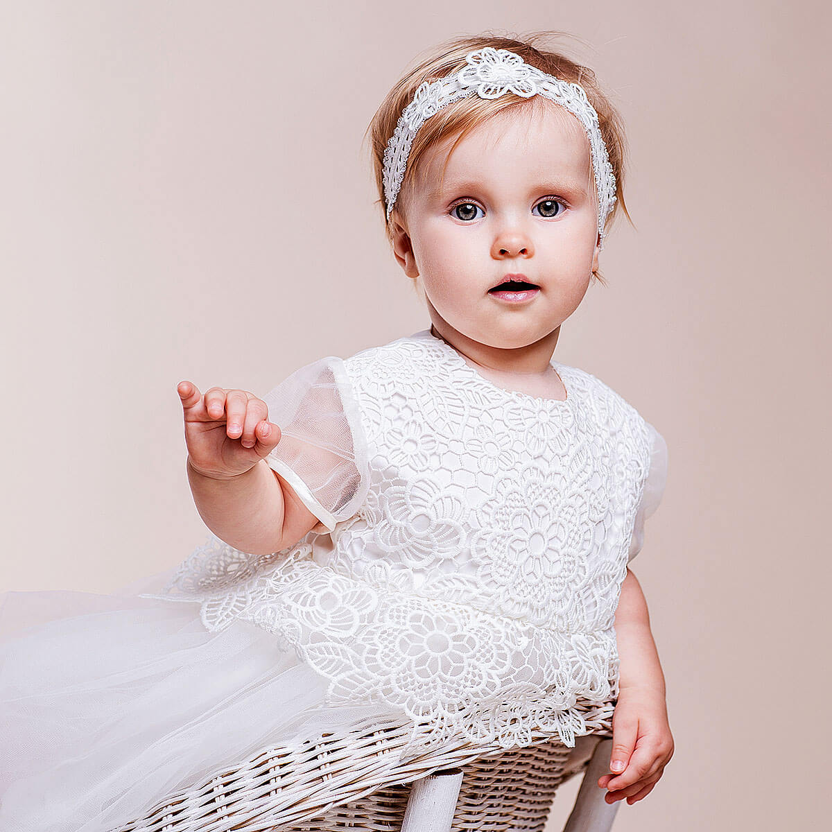 Baby in a Christening Lace Dress with a headband against a beige background