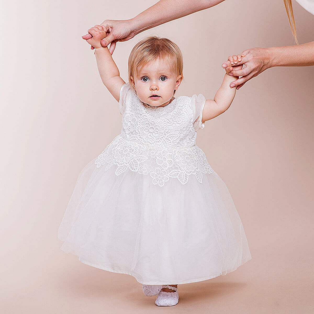 Child in a Christening Lace Dress being held by two hands against a beige background
