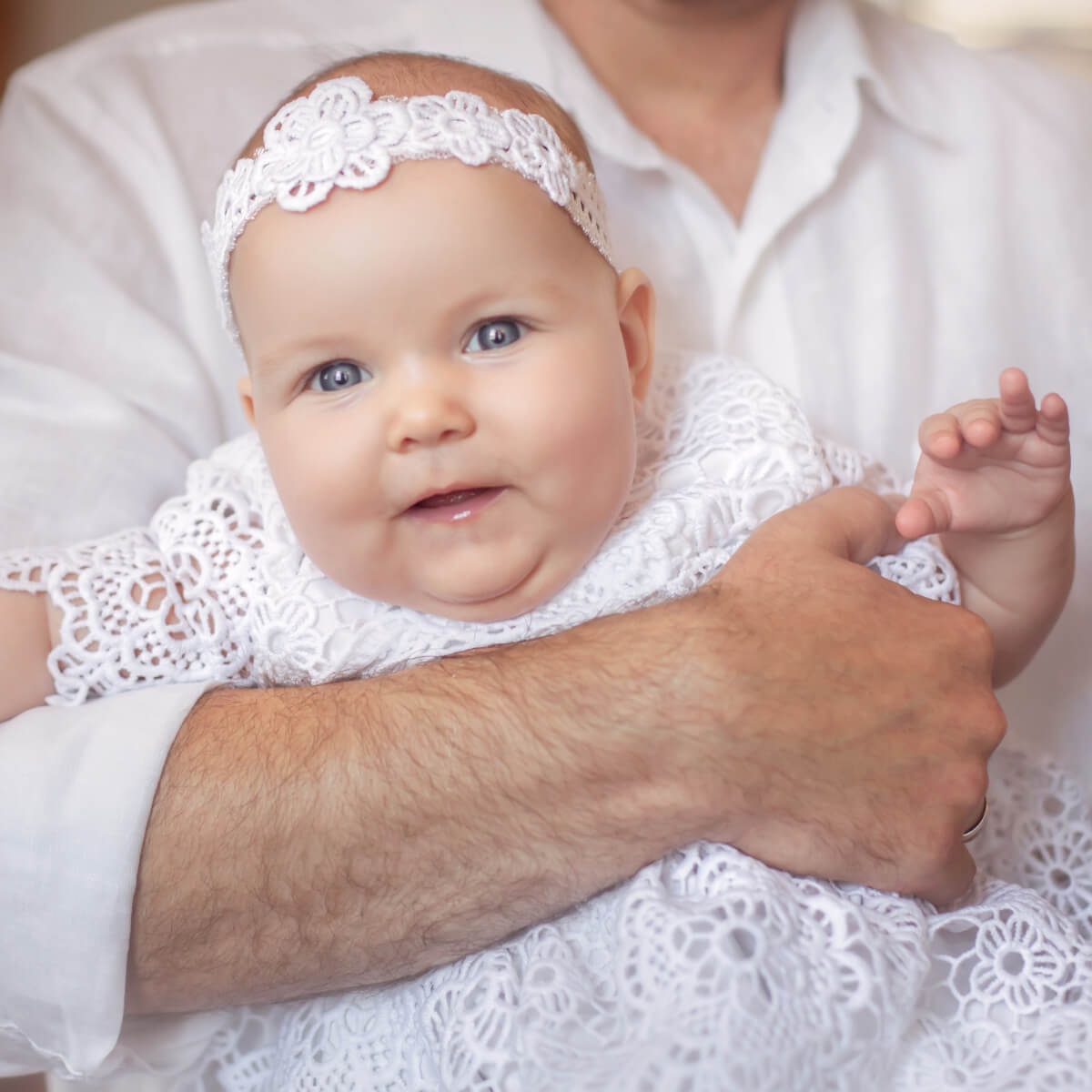 Girl in a white outfit with a baby headband held by an adult