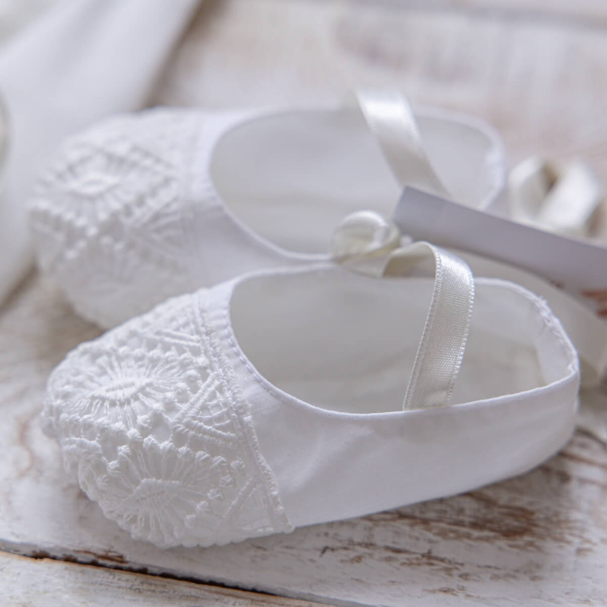 White baby shoes of Baptism Dress Set for Girl with lace details on a wooden surface