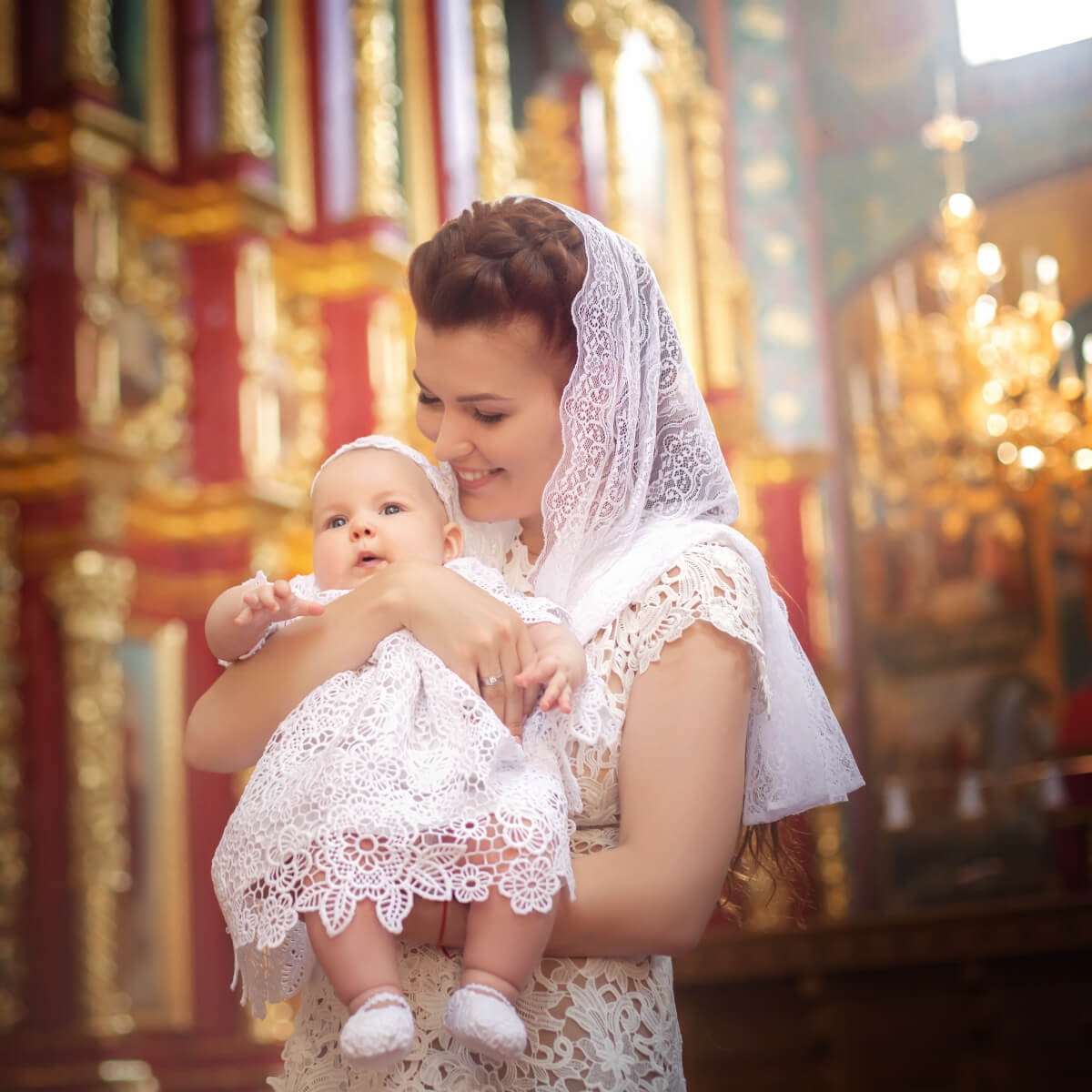 Woman holding a baby in a Lace Baptism Dressr, possibly a church.