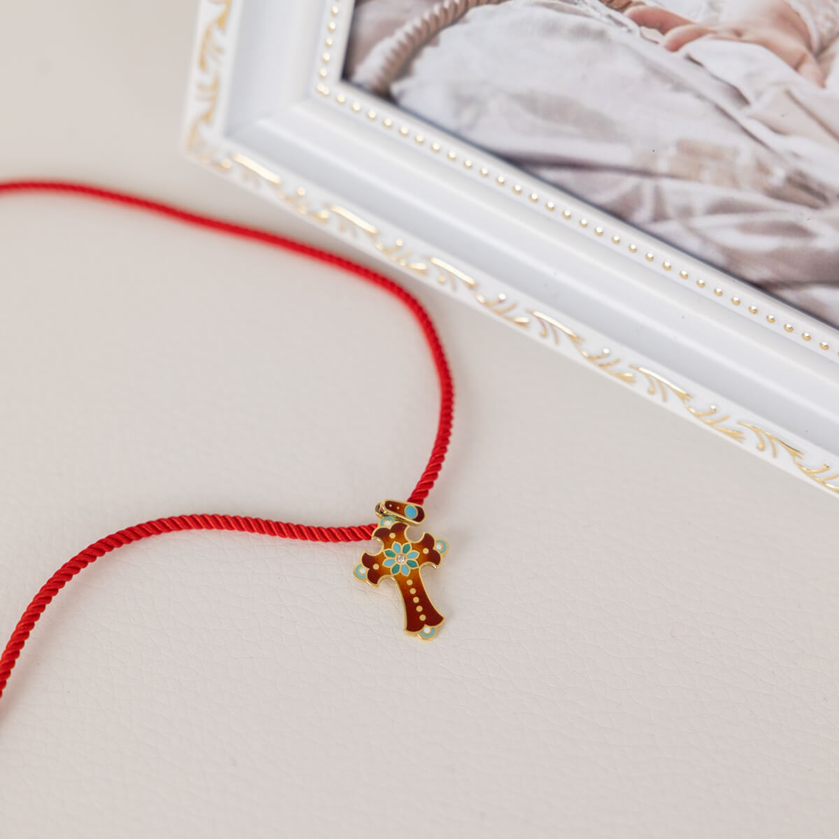 Red string bracelet with a gold cross charm on a light background