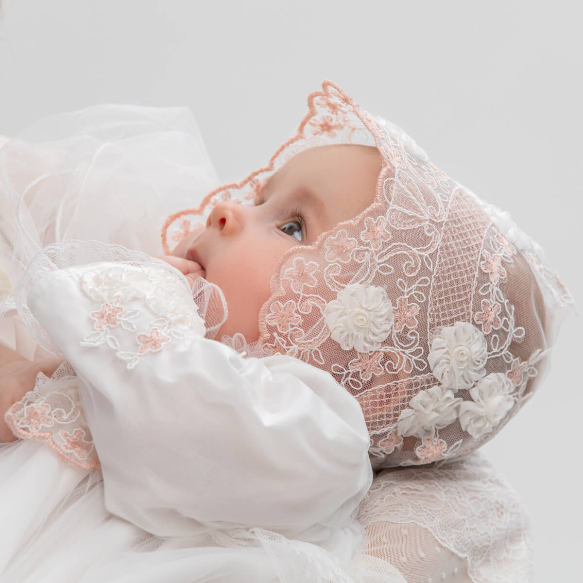 Baby wearing a flower lace baptism bonnet on a light background