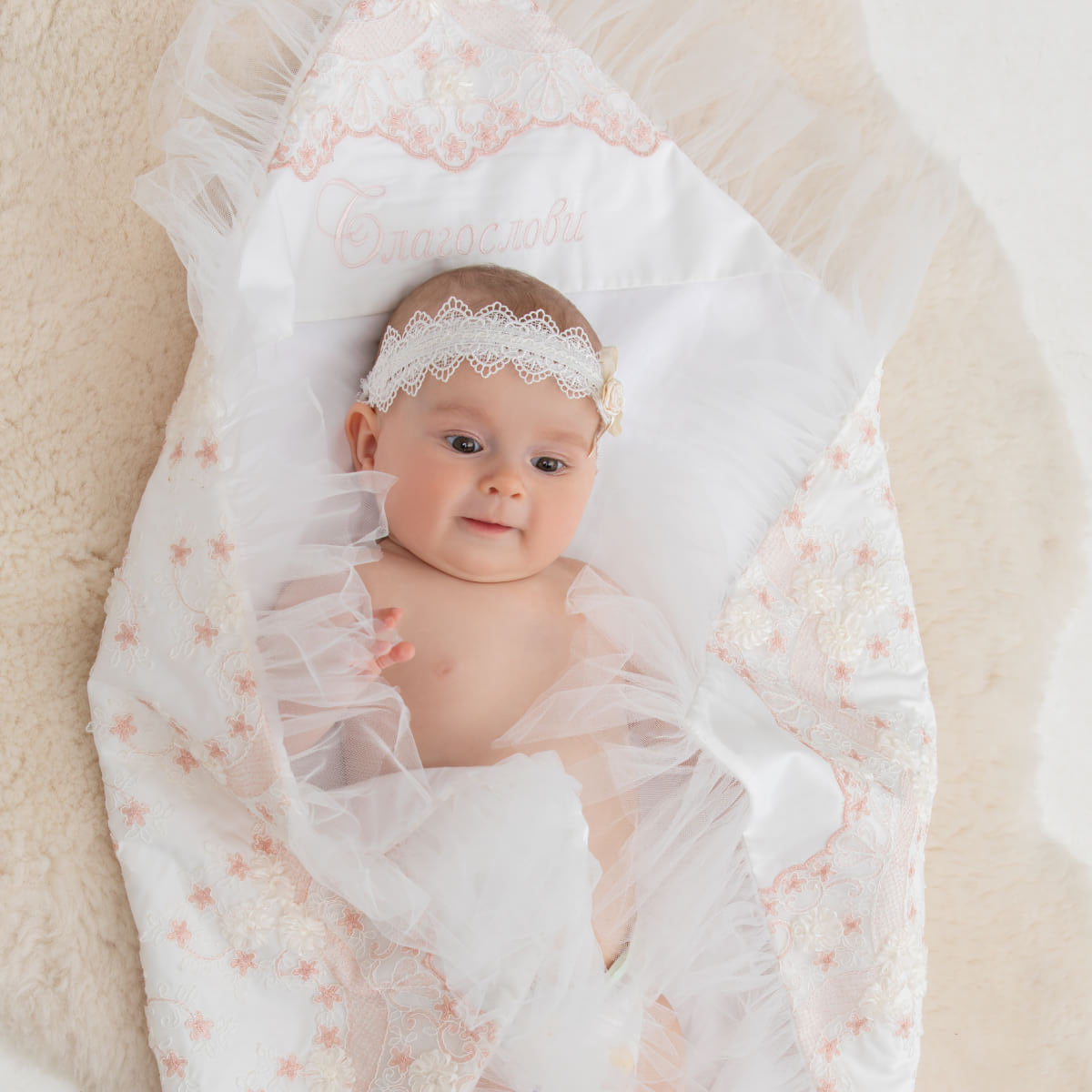 Baby wrapped in a white and pink floral blanket with a headband on a light background