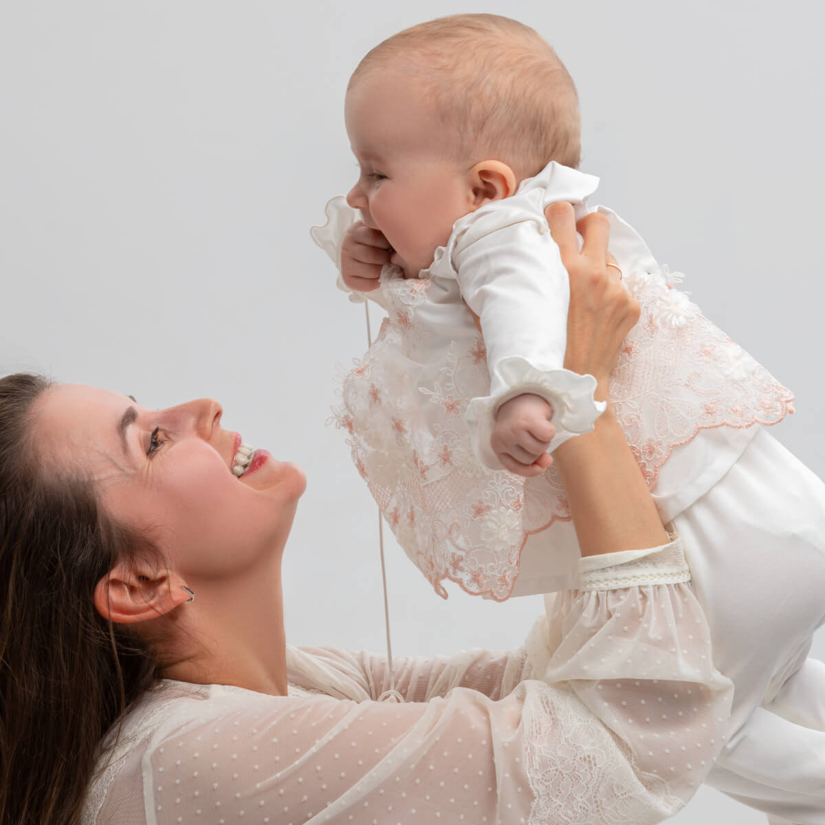 Woman holding a baby dressed in Coming Home Outfit against a light background